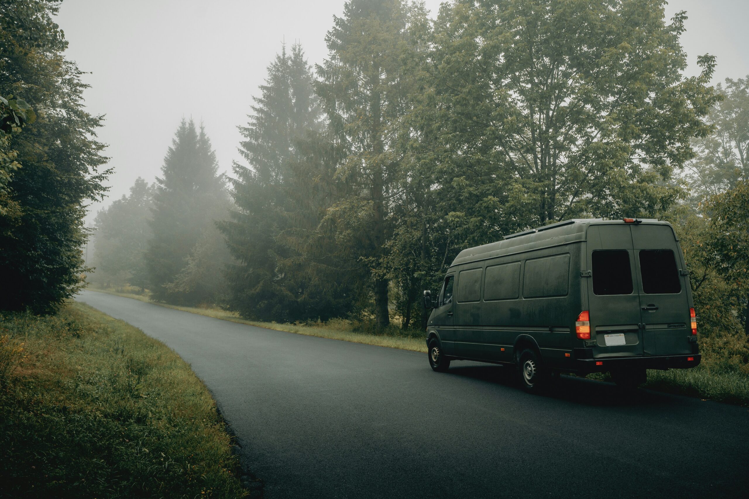 A van a foggy and forested road.